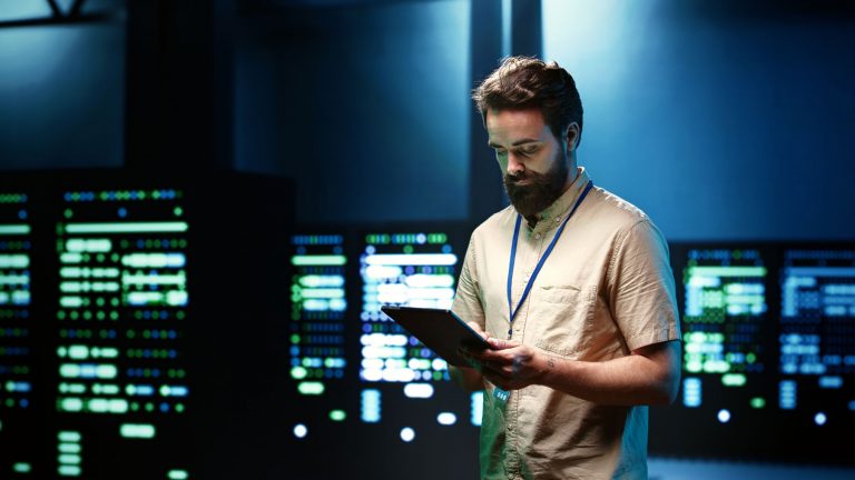 Cyber security consultant looking at tablet, surrounded by IT servers