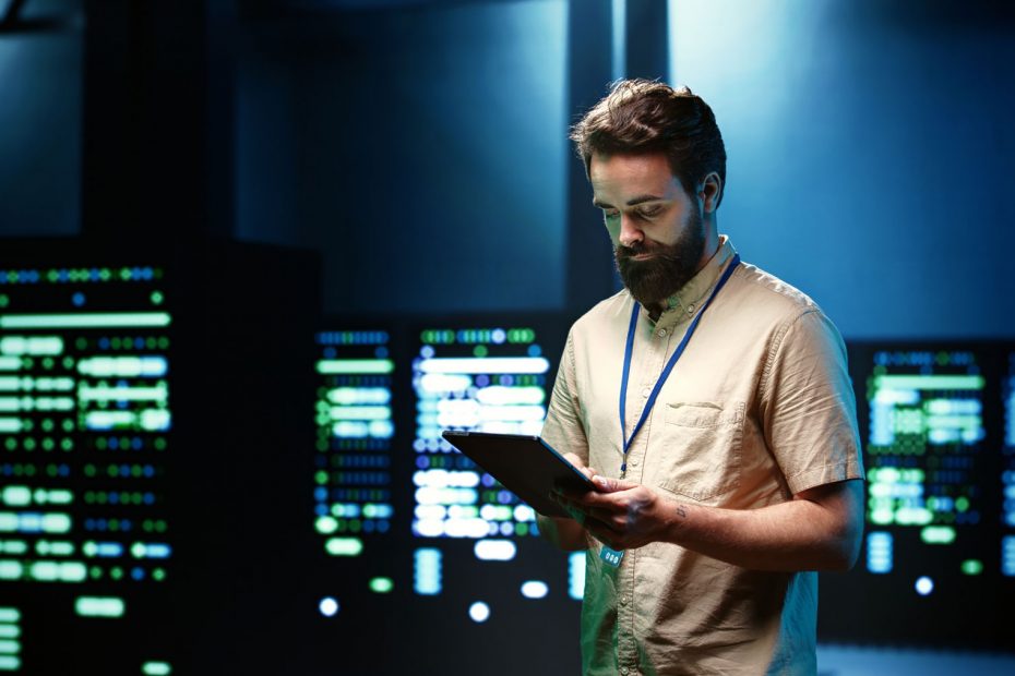 Cyber security consultant looking at tablet, surrounded by IT servers